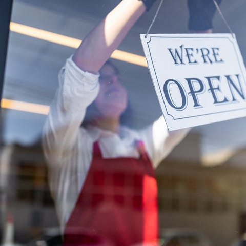 Woman in red apron hanging We're Open sign.