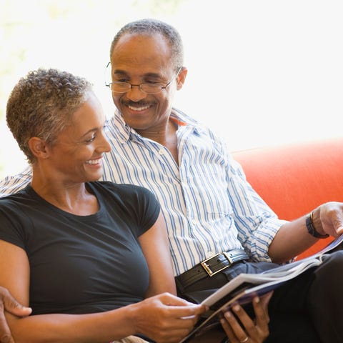 Two smiling people on couch looking at magazine.