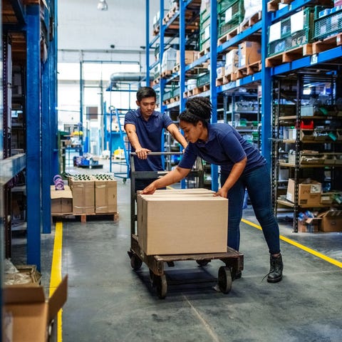 Two warehouse workers with boxes on a cart.
