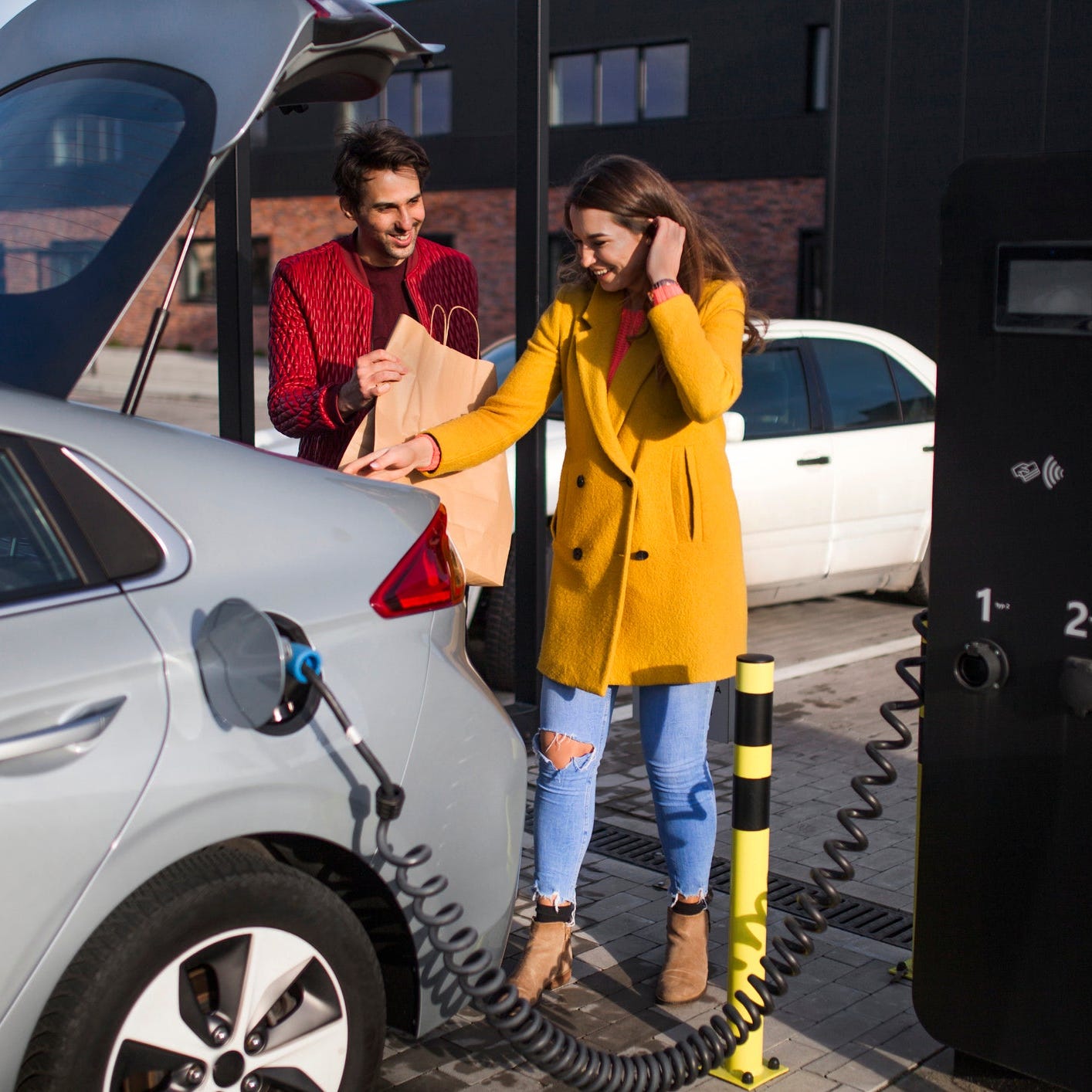 EV owner stores shopping bags in trunk as car is charging.