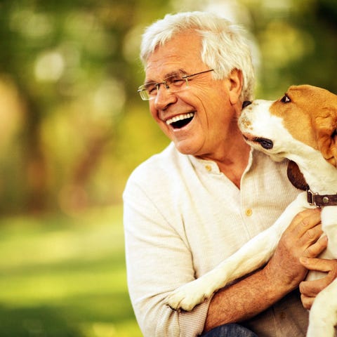 A smiling older man outdoors holding a dog..