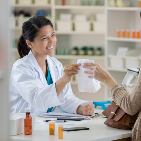 A person at a pharmacy counter hands a white bag t