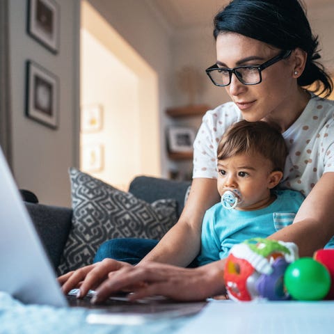 Person holding toddler and using laptop.