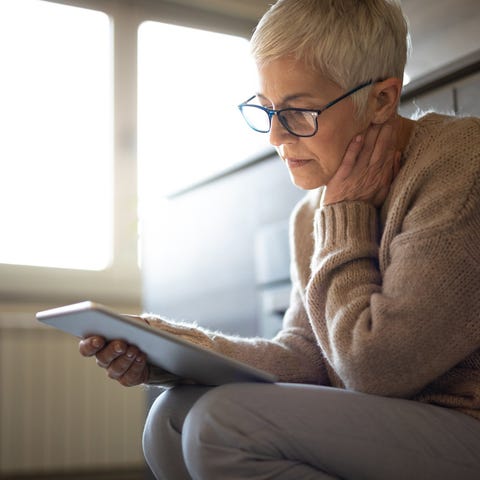 Older person sitting inside looking at a tablet.