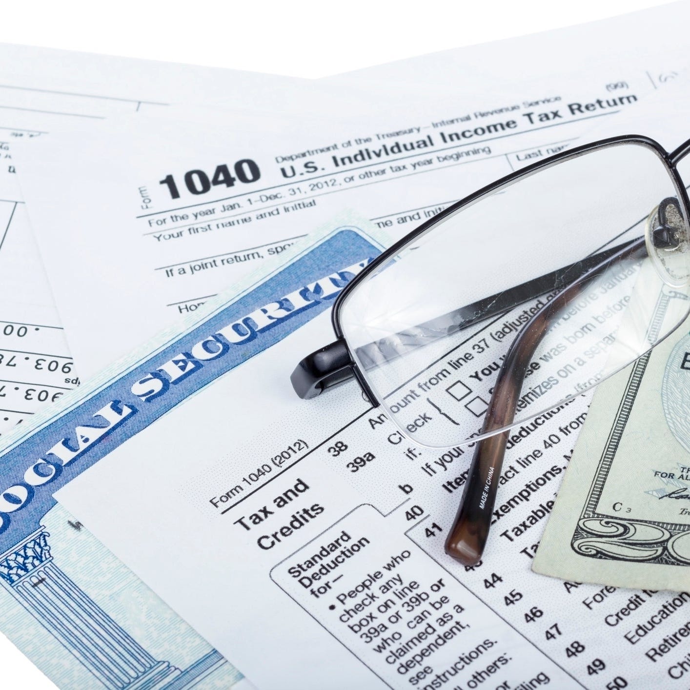 A Social Security card wedged between U.S. tax forms, with eyeglasses and a twenty-dollar bill set atop the tax forms.