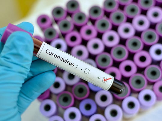 Gloved hand holding a vial of blood with a label that has Coronavirus printed on it