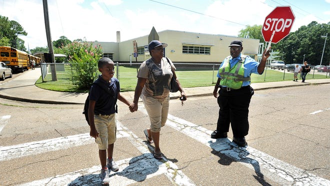 This file photo shows Crossing guard Walter Cheatham stopping traffic on Northside Drive in front of Boyd Elementary School in Jackson as Chicana Nelson walks her son, Lazeric Bullock, home from school.