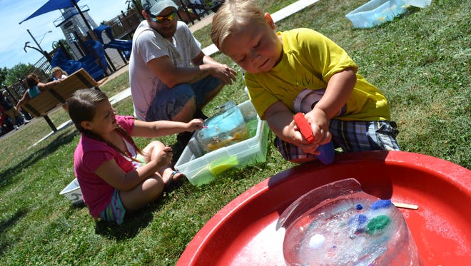 Chloe Carter, 8, and her brother, Leeam Carter, 4, extract toys out of ice as their father, Travis Carter, watches during the Popsicles in the Park event at Lakeview Park hosted by Ottawa County Early Intervention.