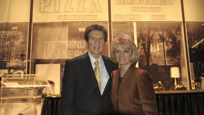 Mike and Marian Ilitch celebrate the 50th anniversary of Little Caesars, which began in 1959 with their Garden City, seen behind them. The company has grown into thenation’sthird-largest pizza chain, behind Pizza Hut and Domino’s.