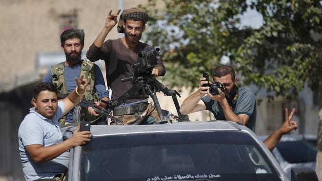Turkish-backed Syrian opposition fighters cheer from a car as they drive around the border town of Akcakale, Sanliurfa province, southeastern Turkey, on their way to Tal Abyad, Syria, Monday, Oct. 14, 2019. Syrian troops entered Monday several northern towns and villages getting close to the Turkish border as Turkey's army and opposition forces backed by Ankara marched south in the same direction raising concerns of a clash between the two sides as Turkey's invasion of northern Syria entered its sixth day. (AP Photo/Lefteris Pitarakis)