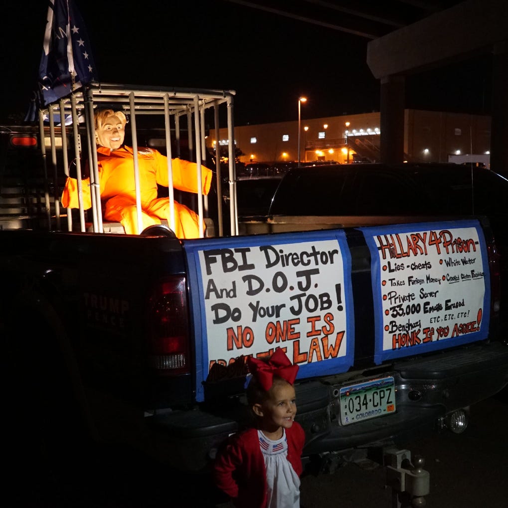 A young girl poses for a picture outside the Trump rally by a pickup showing an effigy of Hillary Clinton locked behind bars.