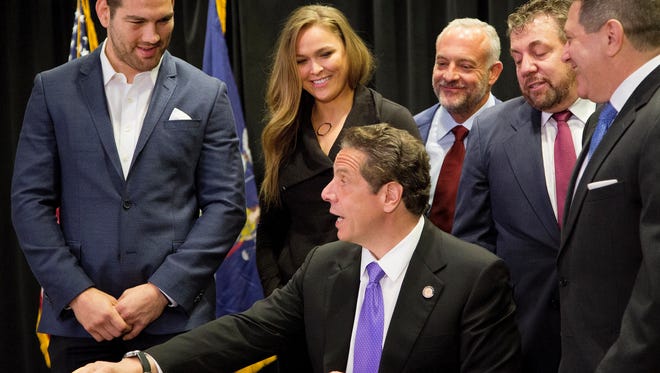Gov. Andrew Cuomo, center, reaches for a pen as he signs into law a measure that will allow professional mixed martial arts in New York, Thursday, April 14, 2016. Behind him are UFC athletes Chris Weidman, left, and Ronda Rousey, and James Dolan, second from right, executive chairman of Madison Square Garden. New York was the last U.S. state to prohibit the bouts. (AP Photo/Mark Lennihan)