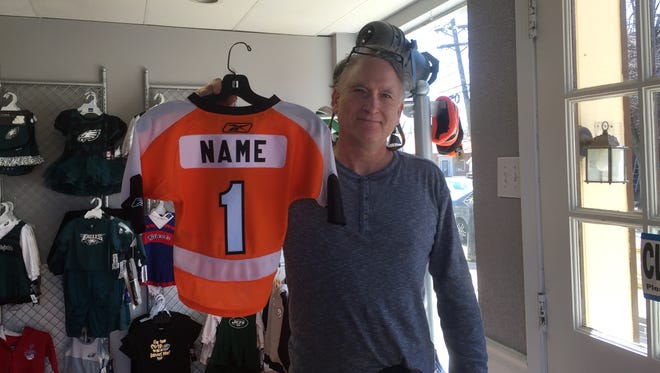 Allen Schwartz shows a kid's Flyers jersey that can be customized in his Haddonfield store, Hello Sports Fans.
