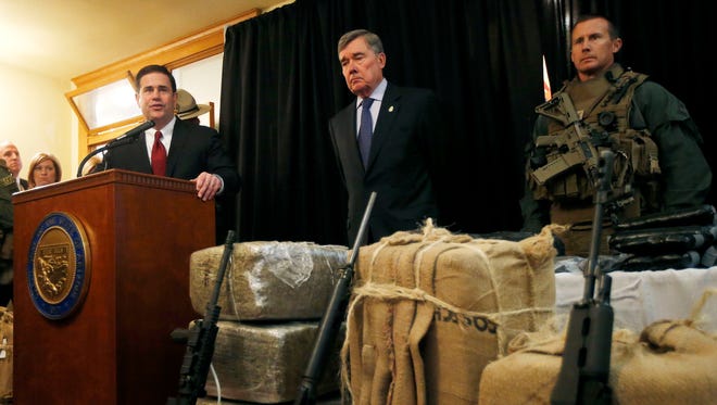 With seized drugs and weapons from border-crossing drug smugglers, Arizona Gov. Doug Ducey, left, speaks at a news conference after testifying at a field hearing of the U.S. Senate Homeland Security and Governmental Affairs Committee at the Arizona Capitol Monday, Nov. 23, 2015, in Phoenix.  R. Gil Kerlikowske, center, commissioner of the U.S. Customs and Border Protection, listens in during the news conference.