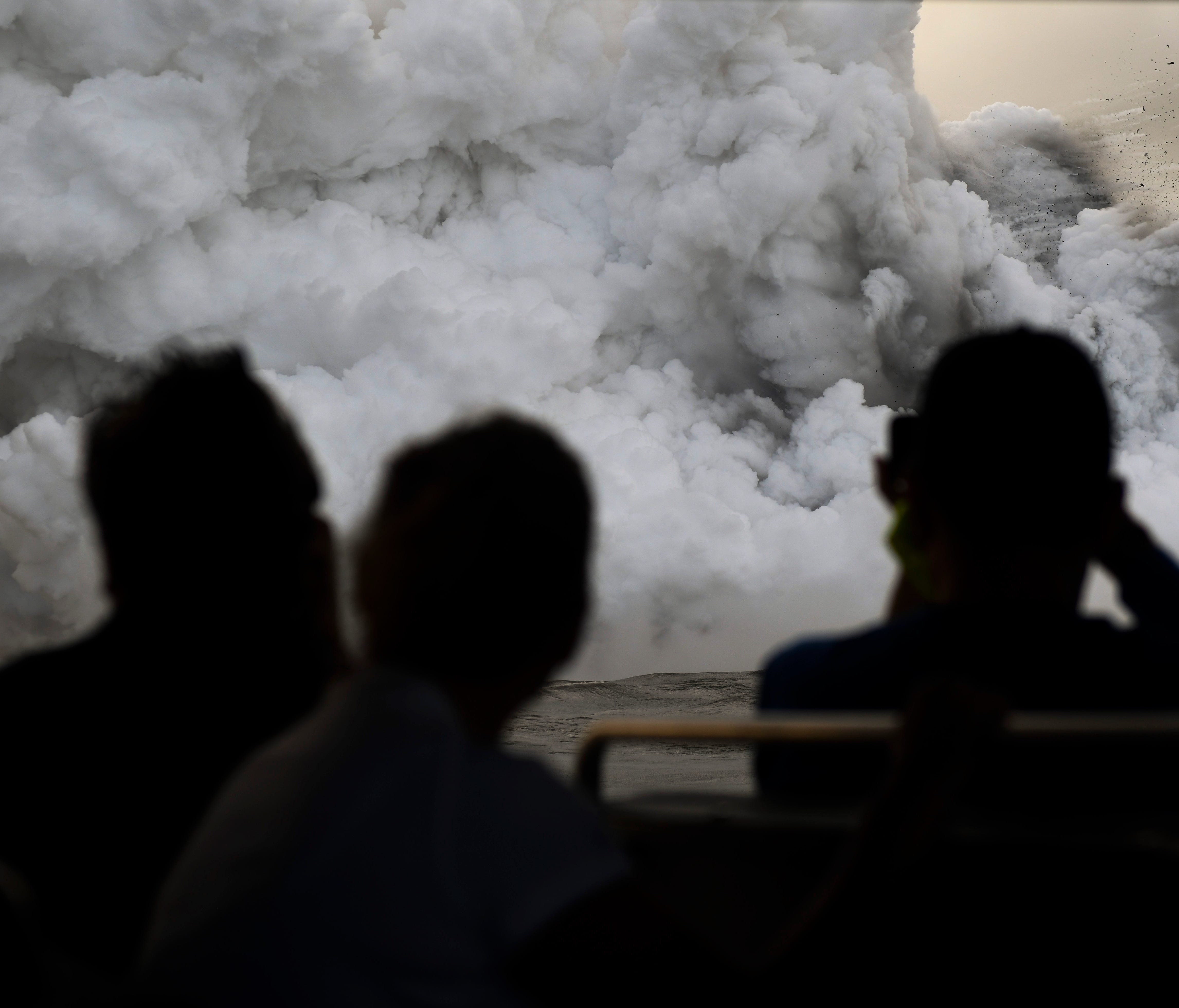 Tourists take photos of steam rising from the entry point where lava from the Kilauea volcano hits the Pacific Ocean. The Kilauea volcano erupted on May 3, with the lava flow destroying 24 homes and causing the evacuation of 2,000 people.