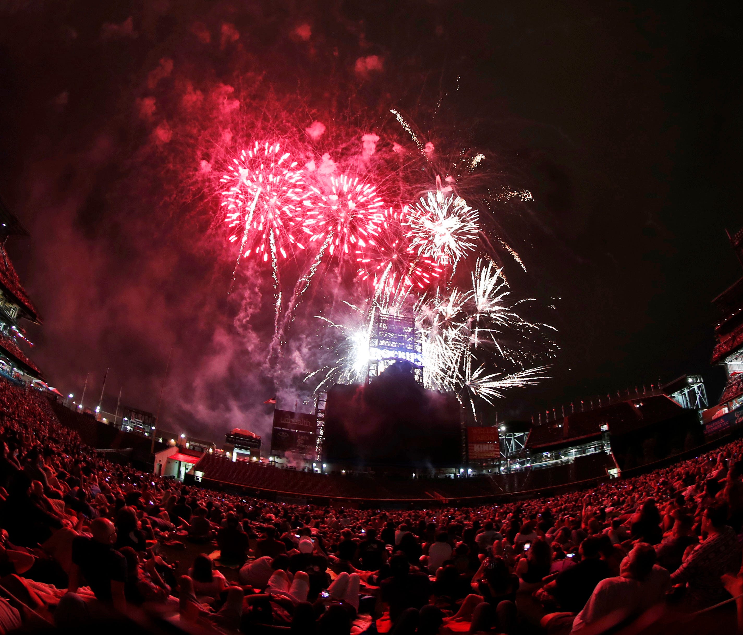 Fireworks to mark the Fourth of July holiday explode as fans sit on the outfield grass of Coors Field after a baseball game Tuesday in Denver.