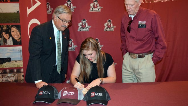 Kaylee Bruhn, of Logan, N.M., signs a certificate of commitment during the ACES Aggie Signing Day ceremony. Watching her sign are College of Agricultural, Consumer and Environmental Sciences Dean Rolando Flores, left, and Jerry Hawkes, assistant dean of academics.