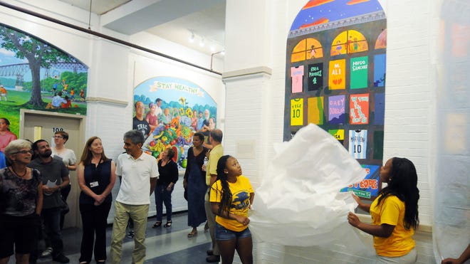 Mionna Chambers, 16, center, and Kiara Allen, 16, unveil on of several new murals at the Family Partnership Center on Thursday in the City of Poughkeepsie.