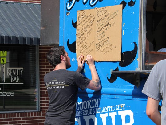 Ryan Hunt, one of the employees of the Moustache Mobile, writes out the menu for Saturday’s Food Truck Festival.