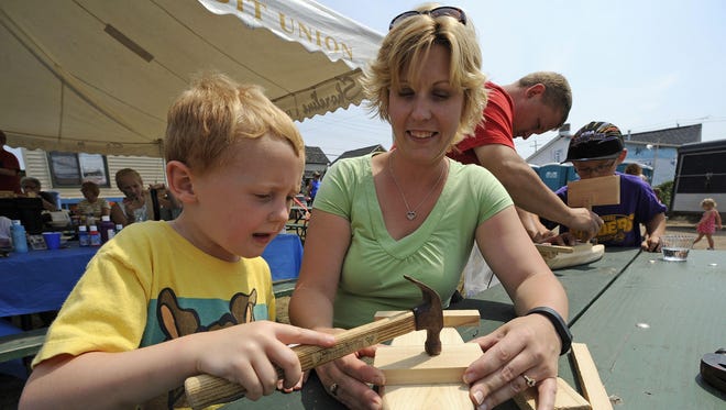 File - Nicole Essert helps son Kaden Essert as husband and father John Essert, back, helps son Sean Essert, all of Two Rivers, as they build wooden boats at Rogers Street Days in Two Rivers.