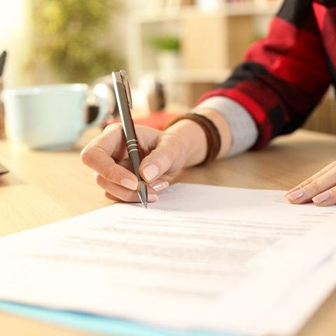 A woman's hands signing paperwork on a desk in a s
