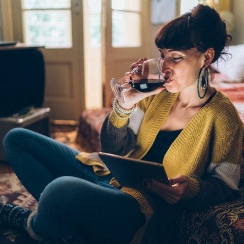 A woman sitting on the floor drinking wine while w