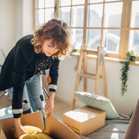 A woman packing moving boxes in a sunny apartment.