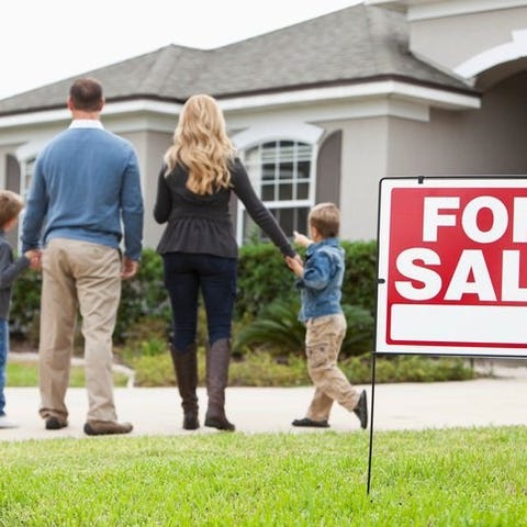 A family looks excitedly at a home with a For Sale