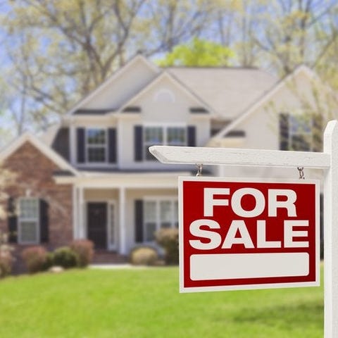 A For Sale sign in front of a two-story house surr