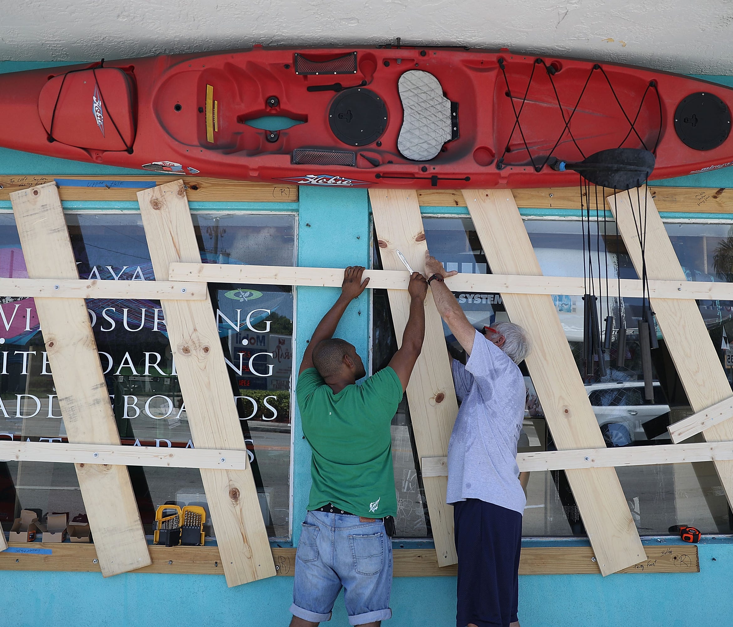 Jim DeSilva, left, and Milton Ibanez put window protection on their business, Sandy Point, as they prepare for Hurricane Irma in Miami.