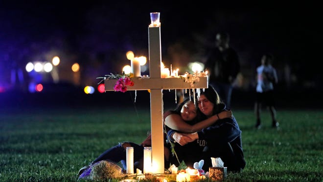Two people comfort each other as they sit and mourn at one of seventeen crosses, after a candlelight vigil for the victims of the Wednesday shooting at Marjory Stoneman Douglas High School, in Parkland, Fla., Thursday, Feb. 15, 2018. Nikolas Cruz, a former student, was charged with 17 counts of premeditated murder on Thursday. (AP Photo/Gerald Herbert)