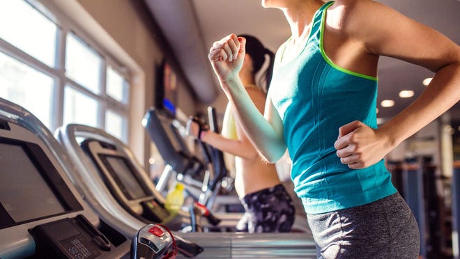 Two women run on treadmills in a gym.