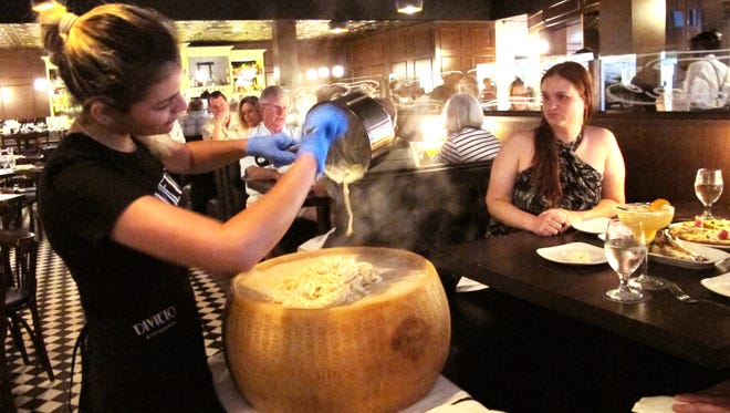 Tableside at Divieto in Coconut Point, Mariana Gonzalez, left, pours hot fettuccine Alfredo atop a huge, aged wheel of cheese to create the restaurant's creamy signature dish Ruota di Parmigiano. (Daily News file)