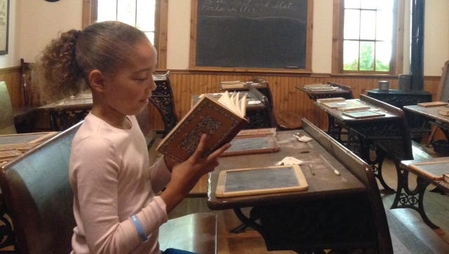 Chloe Scott, 8, of Webster examines an old-fashioned schoolbook at the Webster Museum on Saturday.