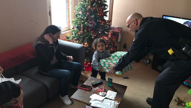 A tiny tot is presented a big Christmas gift by West Allis Police Corp. Rod Nelson. He was helping distribute Christmas gifts to 20 deserving families. The gifts were paid for with a $2,000 anonymous donation, given for that very purpose. Police also shopped for the gifts and wrapped them.