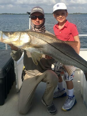 Cooper Symon (right), 8, of Hoboken, N.J., fished Tuesday with Capt. Billy Davenport Jr. (left), of Vero Tackle and Marina, to catch and release this 39-inch, 27-pound snook in the Indian River Lagoon on 10-pound test line. Symon used a live shrimp to record the remarkable catch.