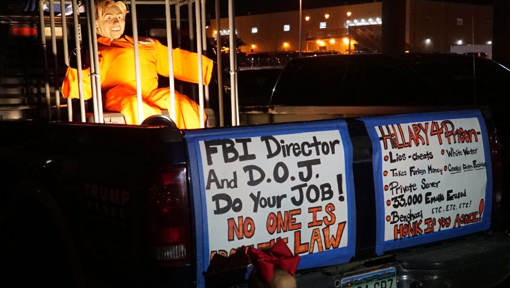 A young girl poses for a picture outside the Trump rally by a pickup showing an effigy of Hillary Clinton locked behind bars.
