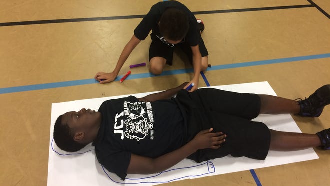 Daveon Johnson looks on as Korde' Adams traces around Johnson on a sheet of paper during an exercise during an antibullying program Jackson Careers & Technology Elementary on Thursday.