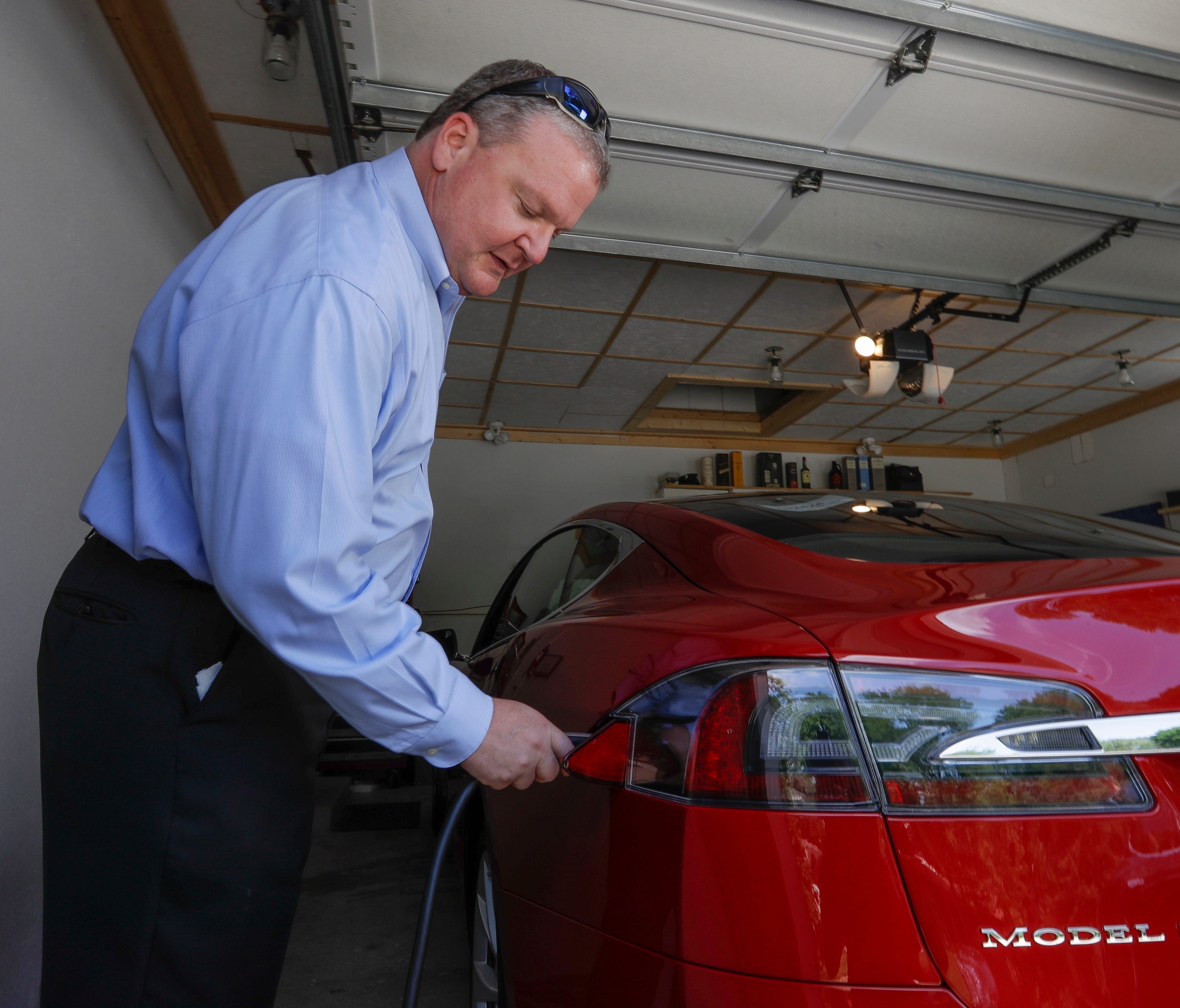 In this Thursday, July 13, 2017, photo, Jeff Solie plugs in his electric Tesla sedan at his home, in New Berlin, Wis. Electric cars are seeing growing support around the world.  But there's a problem: There aren't enough places to plug those cars in.