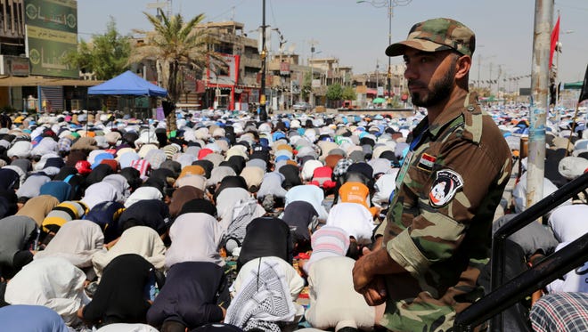 A Shiite fighter stands guard over followers of Shiite cleric Muqtada al-Sadr attending open-air Friday prayers in the Shiite stronghold of Sadr City, Baghdad, Iraq.
