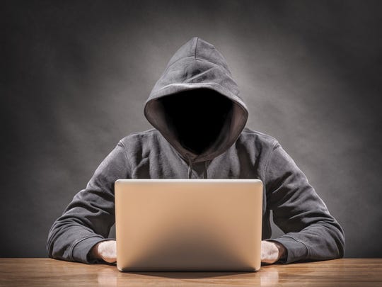 Someone in a hooded sweatshirt on a laptop, illustrating cybercrime.