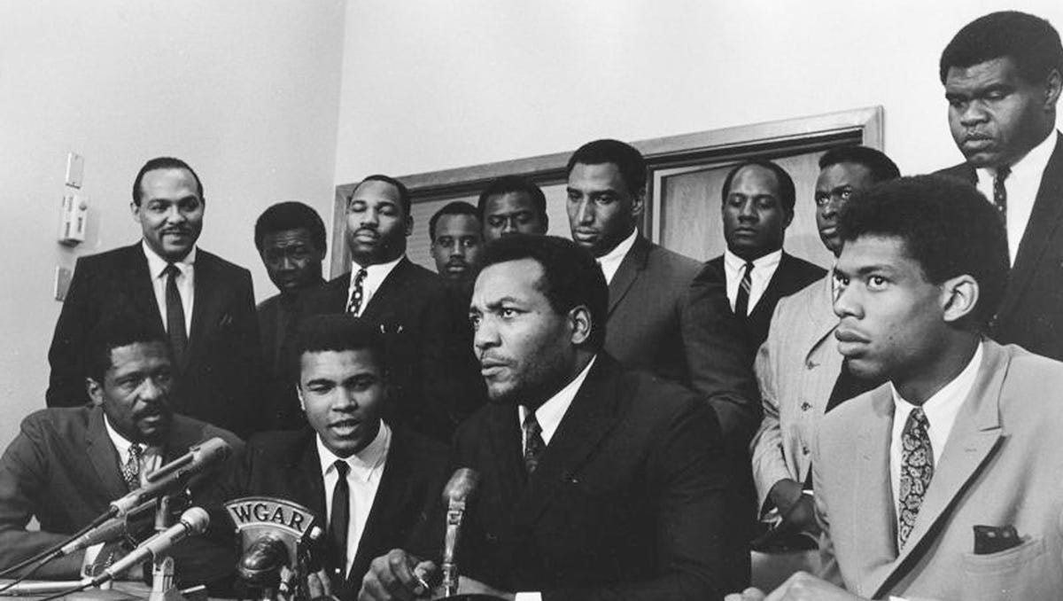A group of top African-American athletes gathers in 1967 to give support for boxer Muhammad Ali, who rejected the draft during the Vietnam War. Seated in the front row, from left to right: Bill Russell, Muhammad Ali, Jim Brown and Kareem Abdul-Jabbar (then Lew Alcindor). Standing behind them are: Carl Stokes, Walter Beach, Bobby Mitchell, Sid Williams, Curtis McClinton, Willie Davis,   Jim Shorter, and John Wooten.