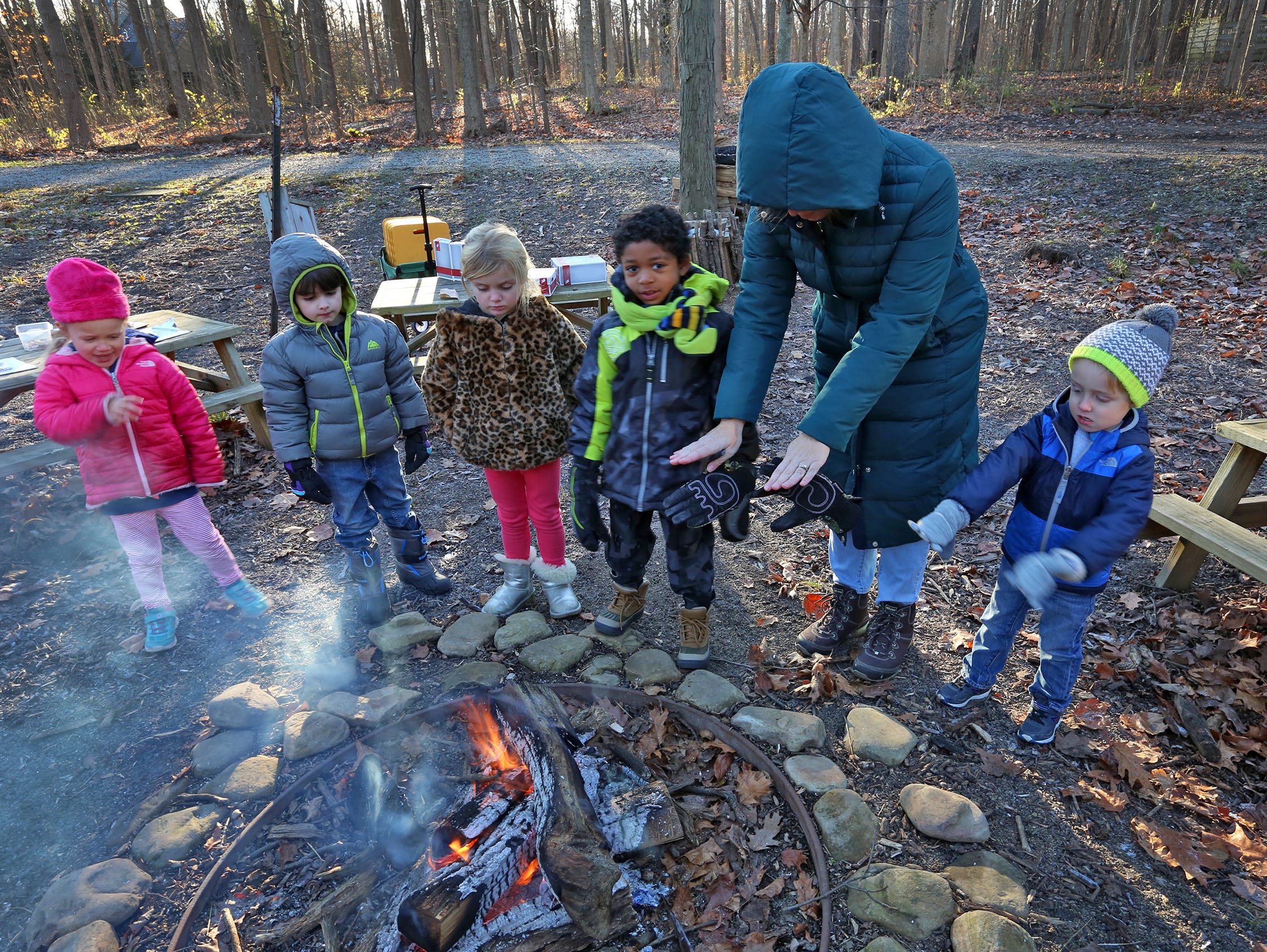 Melissa Jackson warms herself at the fire with kids during an outdoor learning time at The Orchard School, Wednesday, Dec. 6, 2017.  The northern-Indianapolis charter school commits to learning outside for at least two hours every day.