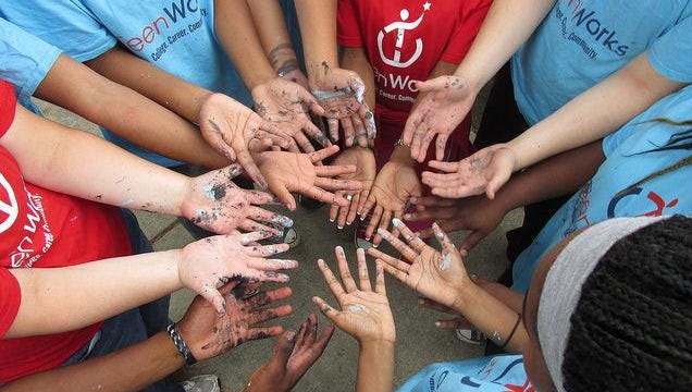 Participants in TeenWork’s Great Place Near East work-site group show the paint on their hands, after they helped paint over the boards covering the doors and windows of abandoned houses in Indy’s Near-Eastside neighborhood.