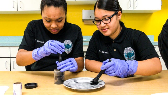 Cristina DeSilva and Alondra Olavarria, juniors at East Lee County High School, work on lifting fingerprints from a plate using magnetic dust and a wand during class Friday, Feb. 23, 2018. FMPD's CSI employees were at East Lee County High School to demonstrate their jobs to the students in the criminal justice academy. This is part of the FMPD's partnership with the school district to help recruit more locals to join the police force.