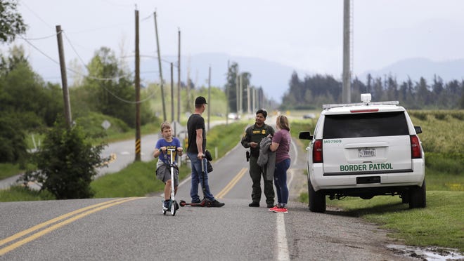 In this photo taken May 17, 2020, a Border Patrol officer in the U.S. talks with nearby residents on E. Boundary Rd., paralleling 0 Ave. behind them in Canada, near Lynden, Wash. With the border closed to nonessential travel amid the global pandemic, families and couples across the continent have found themselves cut off from loved ones on the other side.