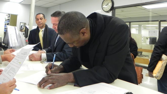 Jeffrey Dye, at right, signs his ballot form to run for Passaic City Council member, with Diaz, center, who will run for mayor on a joint ticket. Diaz's friend Ramon Pena, left, looks on.