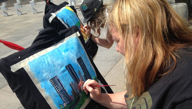 Patient advocate Regina Holliday paints a picture for a jacket for information technology executive Alice Lovey in front of the Department of Health and Human Services in May during a protest. The towers spell HIT for health information technology. People wear the paintings, which tell their healthcare stories, on jackets.