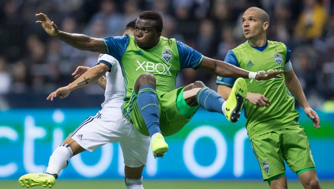 Seattle Sounders' Nouhou, front, of Cameroon, falls to the ground after kicking the ball away from Vancouver Whitecaps' Cristian Techera, back left, of Uruguay, as Seattle's Osvaldo Alonso, of Cuba, watches during the second half of an MLS playoff soccer match in Vancouver, British Columbia, Sunday, Oct. 29, 2017. (Darryl Dyck/The Canadian Press via AP)