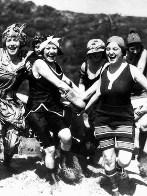 Bathing suit clad ladies drag a reluctant man to the water for a little swim. Undated, probably 1920s.